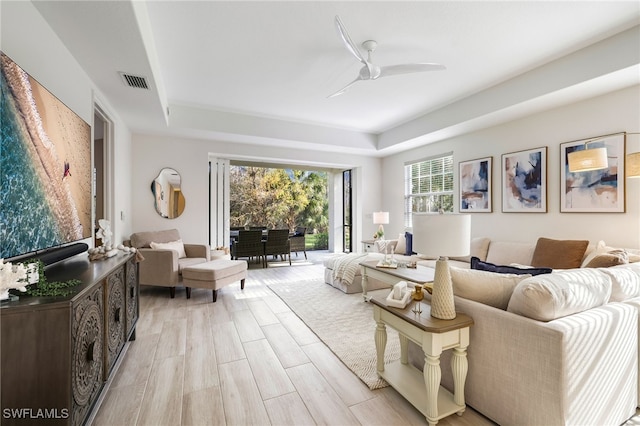 living room with a ceiling fan, a tray ceiling, light wood-style floors, and visible vents