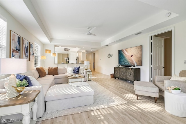 living area featuring ceiling fan, visible vents, light wood-type flooring, and a raised ceiling
