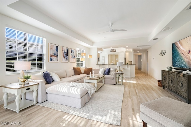 living area with a tray ceiling, visible vents, light wood-style floors, and a ceiling fan