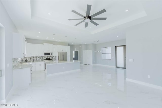 kitchen with appliances with stainless steel finishes, white cabinets, backsplash, a center island, and a raised ceiling