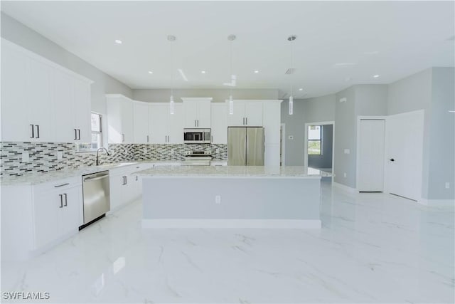 kitchen with white cabinetry, light stone counters, a center island, hanging light fixtures, and appliances with stainless steel finishes