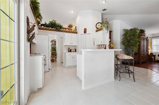 kitchen featuring light tile patterned floors, a peninsula, white cabinetry, light countertops, and a kitchen bar