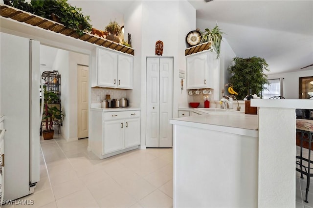 kitchen featuring tasteful backsplash, light countertops, freestanding refrigerator, white cabinets, and a sink