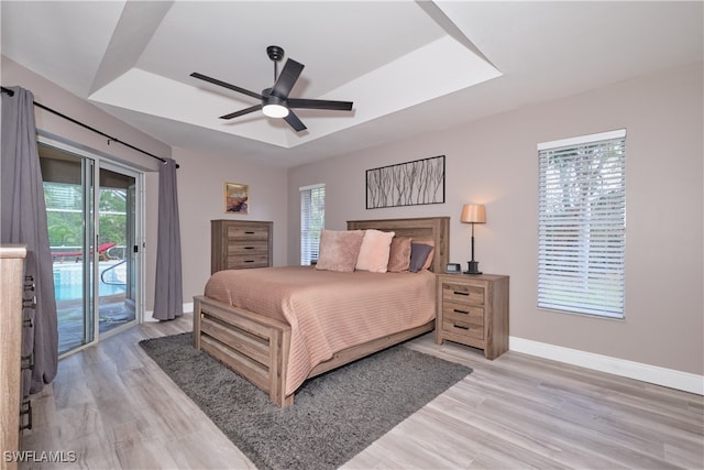 bedroom with ceiling fan, light hardwood / wood-style flooring, a tray ceiling, and access to exterior