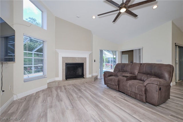 living room with light wood-type flooring, a tiled fireplace, high vaulted ceiling, and ceiling fan