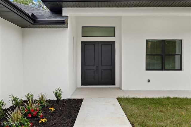 view of exterior entry with roof with shingles and stucco siding