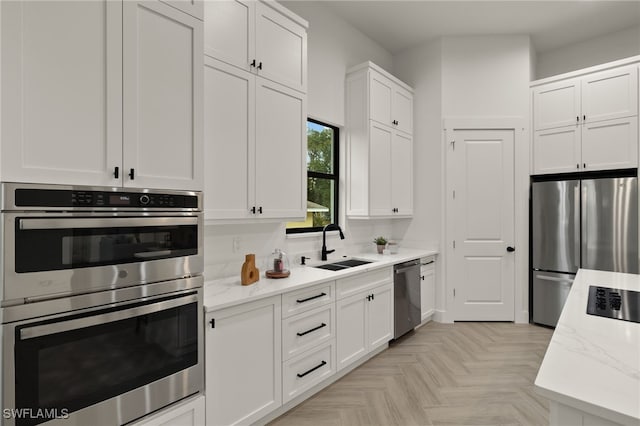 kitchen with stainless steel appliances, light stone counters, a sink, and white cabinetry