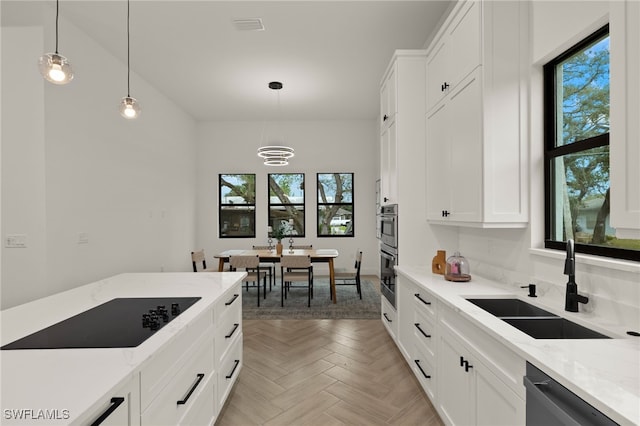 kitchen featuring hanging light fixtures, black appliances, white cabinets, and a sink