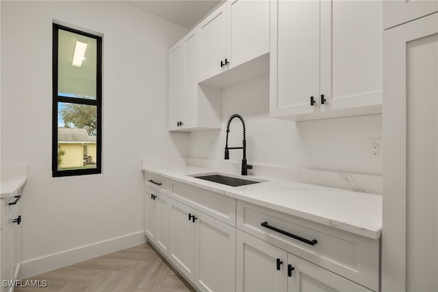 kitchen featuring light stone counters, a sink, white cabinetry, and baseboards