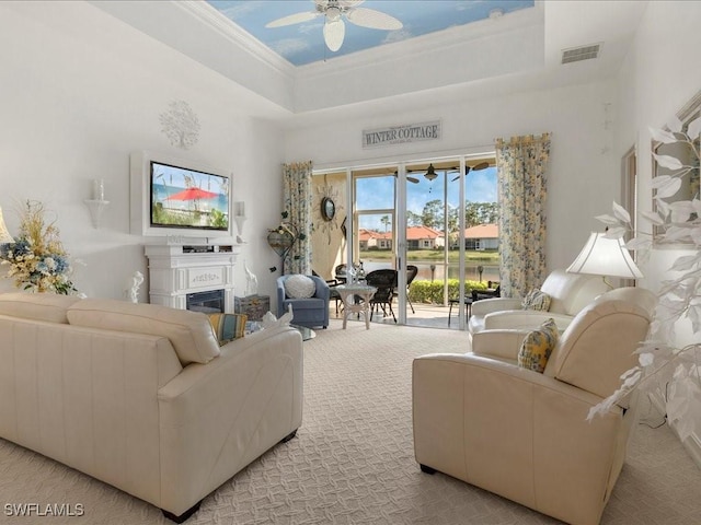 living room featuring a raised ceiling, a glass covered fireplace, visible vents, and light colored carpet