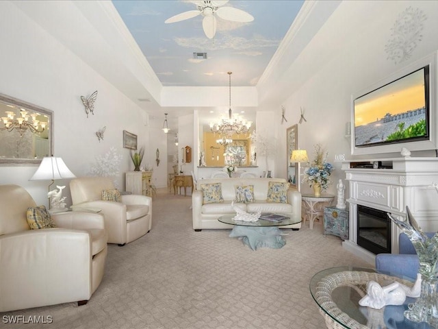 living area with light colored carpet, ceiling fan with notable chandelier, visible vents, a tray ceiling, and a glass covered fireplace