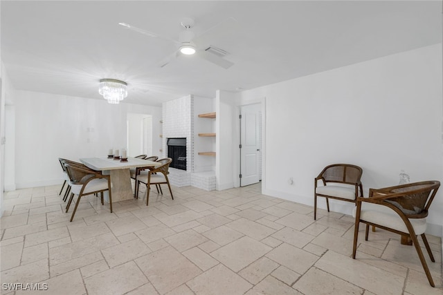 dining room featuring visible vents, ceiling fan with notable chandelier, stone tile floors, baseboards, and a brick fireplace
