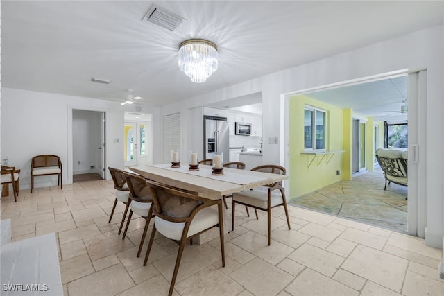 dining room with stone tile floors, ceiling fan with notable chandelier, and visible vents
