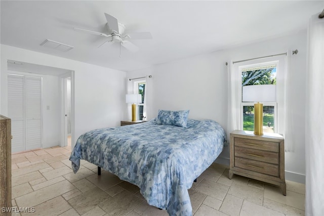 bedroom featuring ceiling fan, visible vents, baseboards, and stone tile flooring