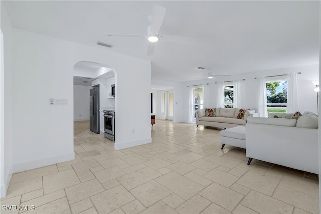 living area with stone tile floors, a ceiling fan, baseboards, visible vents, and arched walkways