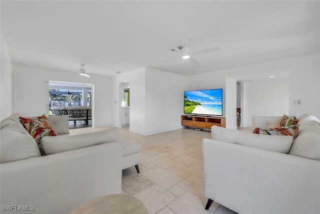 living area with baseboards, arched walkways, stone tile floors, and a ceiling fan