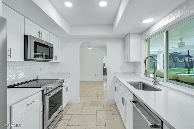 kitchen with stone tile floors, stainless steel appliances, a raised ceiling, a ceiling fan, and a sink