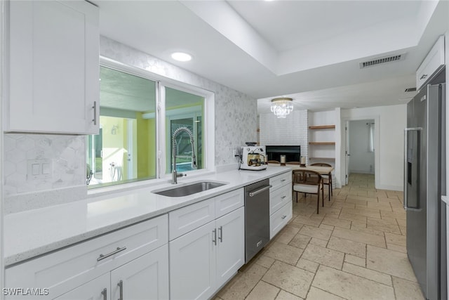 kitchen with appliances with stainless steel finishes, white cabinets, backsplash, a tray ceiling, and sink