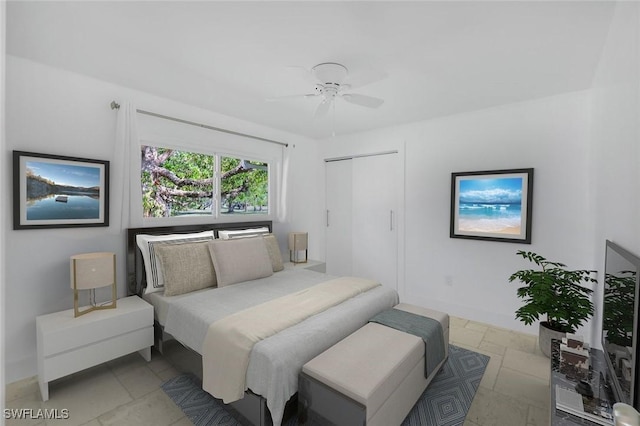 bedroom with stone tile floors, ceiling fan, baseboards, and a closet