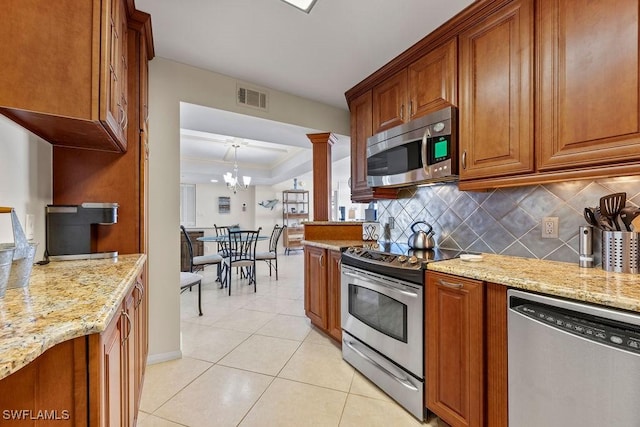 kitchen with a tray ceiling, appliances with stainless steel finishes, tasteful backsplash, and light stone counters