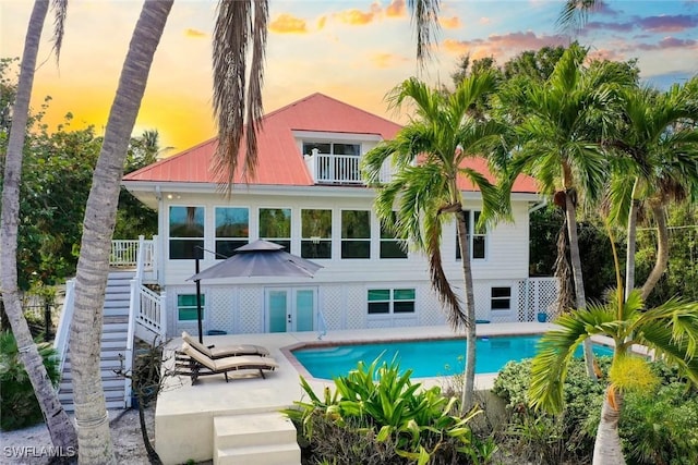 back house at dusk featuring a patio, a fenced in pool, french doors, and a balcony