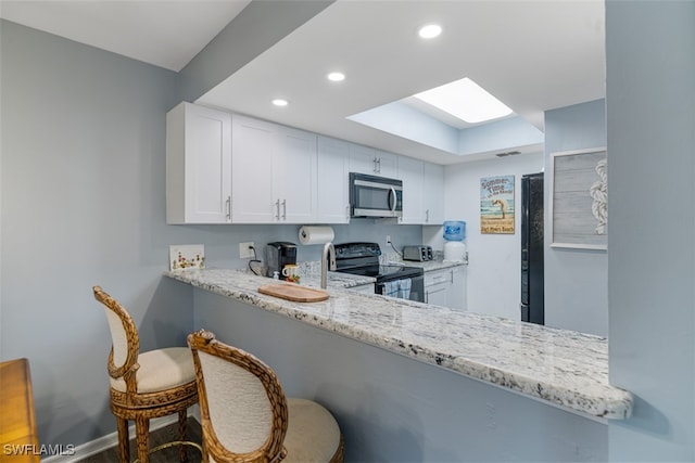 kitchen featuring light stone counters, black range with electric cooktop, white cabinetry, stainless steel microwave, and a kitchen bar