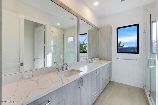 full bath featuring wood finished floors, a sink, baseboards, a marble finish shower, and double vanity