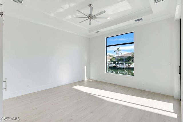 empty room with a raised ceiling, visible vents, ceiling fan, wood finished floors, and baseboards