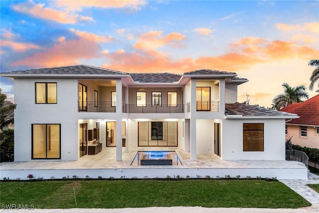 rear view of property featuring a lawn, a patio area, a balcony, and stucco siding