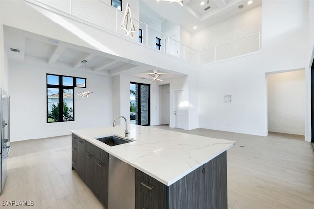 kitchen featuring a sink, baseboards, open floor plan, light wood-style floors, and beam ceiling