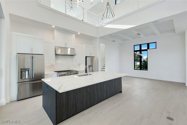 kitchen with stainless steel fridge with ice dispenser, high end fridge, a large island with sink, under cabinet range hood, and a sink