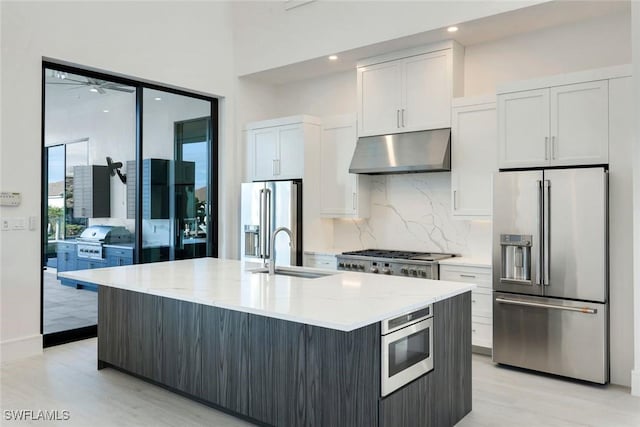 kitchen featuring stainless steel appliances, tasteful backsplash, a sink, light stone countertops, and under cabinet range hood