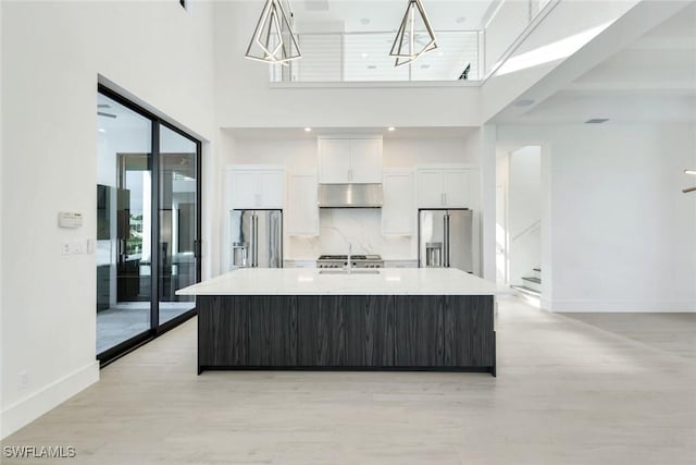 kitchen featuring a sink, white cabinets, high end fridge, stainless steel fridge with ice dispenser, and a center island with sink