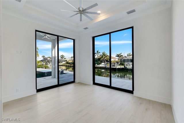 unfurnished room featuring a water view, ceiling fan, a tray ceiling, and wood finished floors