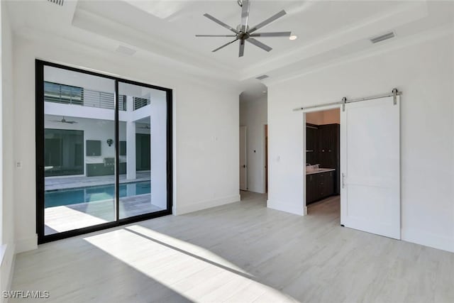 unfurnished room with a barn door, a ceiling fan, baseboards, light wood-type flooring, and a tray ceiling