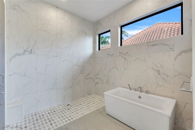 bathroom featuring tiled shower, a freestanding bath, and tile walls