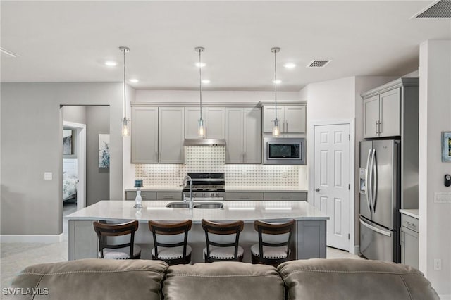 kitchen with gray cabinets, stainless steel appliances, hanging light fixtures, and a center island with sink