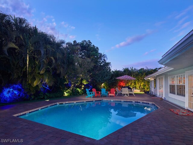 pool at dusk featuring an outdoor pool and a patio