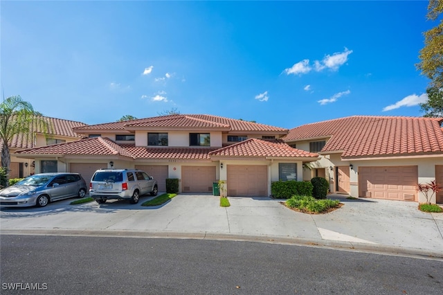 view of front of home featuring driveway, an attached garage, a tile roof, and stucco siding