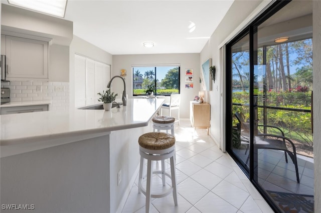 kitchen featuring light tile patterned floors, a sink, light countertops, backsplash, and a kitchen bar