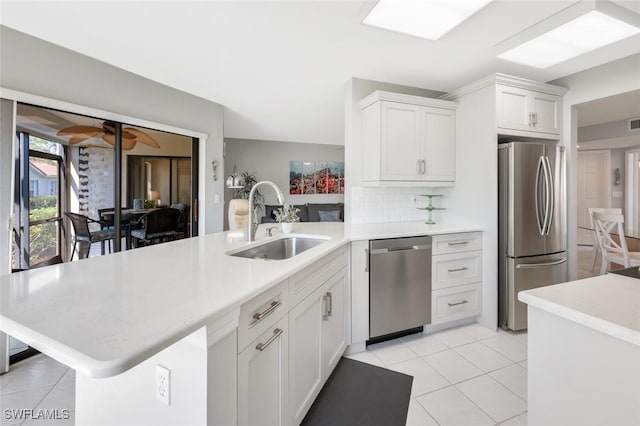 kitchen featuring decorative backsplash, a peninsula, stainless steel appliances, white cabinetry, and a sink