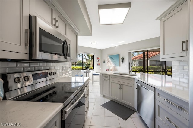 kitchen with light tile patterned floors, tasteful backsplash, gray cabinets, stainless steel appliances, and a sink