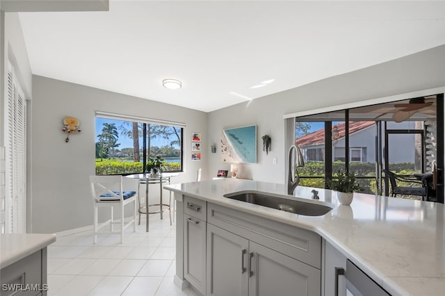 kitchen featuring light tile patterned floors, light stone counters, a sink, and gray cabinetry