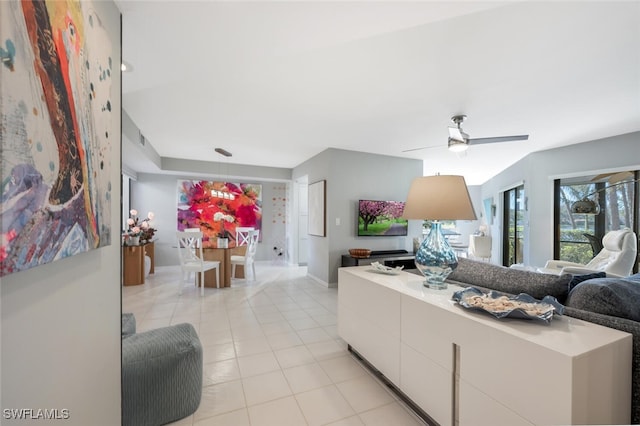 living area featuring light tile patterned flooring, a ceiling fan, and baseboards