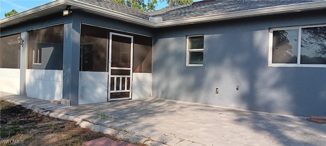 view of side of home featuring roof with shingles, a patio area, a sunroom, and stucco siding