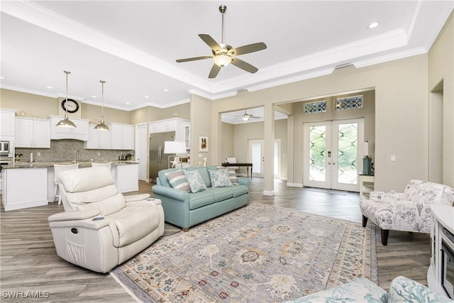 living room with sink, crown molding, a raised ceiling, and french doors