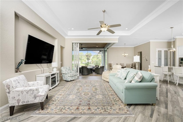 living room with ornamental molding, ceiling fan with notable chandelier, and a raised ceiling