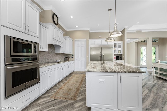 kitchen with built in appliances, white cabinetry, sink, and an island with sink