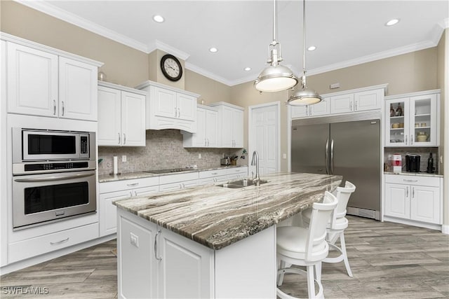 kitchen featuring built in appliances, light stone countertops, sink, white cabinetry, and a kitchen island with sink