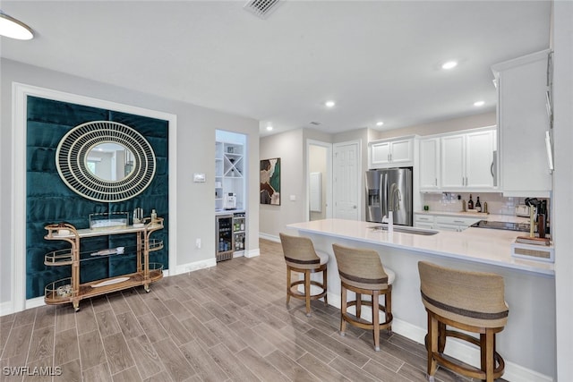 kitchen with a kitchen bar, sink, stainless steel fridge with ice dispenser, kitchen peninsula, and white cabinets